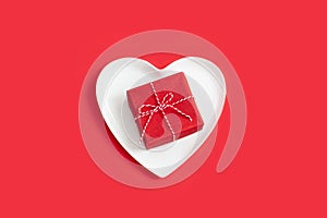 Small red gift box on a white heart-shaped plate.