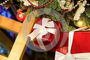 Small red giftbox with a bow on the background of a decorated Christmas tree close-up