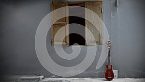 A small red guitar leaning against an old cement wall in vintage tone