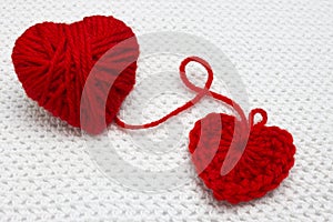 A small red handmade crochet heart and red yarn ball like a heart on the white crochet background. A heart made of wool yarn. Roma