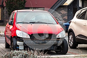 A small red hatchback car with missing frontal par after a traffic accident with radiator visible