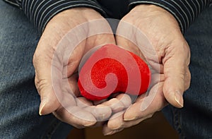 A small red heart in the hands of an elderly man.Concept: the heart is a symbol of love and loyalty.Valentine`s Day.