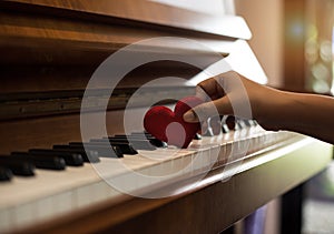 The small red heart was put on piano keys by human hand,warm light tone,reflection of sunlight is shining to piano photo