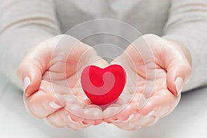 Small red heart in woman`s hands in a gesture of giving, protecting