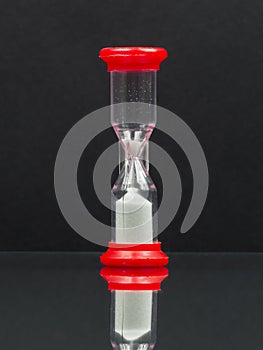 Small red hourglass with white sand and reflexion