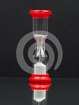 Small red hourglass with white sand and reflexion