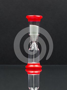 Small red hourglass with white sand and reflexion