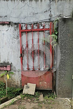 A small red metal door propped against a white wall near a concrete pillar with colored stones.