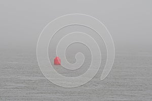 A small red navigation buoy in a foggy ocean