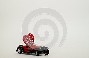 A small red retro bugatti car carries a heart. The Concept Of Valentine`s Day