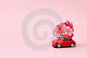 Small red retro toy car with a red and white flower on the roof. Christmas, Valentine`s Day, World Women`s Day