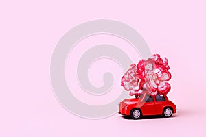 Small red retro toy car with a red and white flower on the roof. Christmas, Valentine`s Day, World Women`s Day