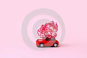 Small red retro toy car with a red and white flower on the roof. Christmas, Valentine`s Day, World Women`s Day