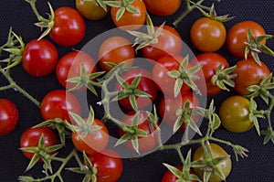 Small red tomatoes with calyxes on black floor