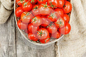 Small red tomatoes in a wicker basket on an old wooden table. Ripe and juicy cherry and burlap cloth, Terevan style country style