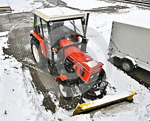 Small red tractor with snow plow for street cleaning in winter season