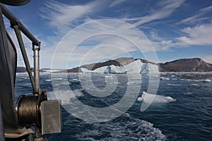 A small research vessel navigates around icebergs in a fjord in Greenland