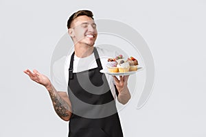 Small retail business, coffee shops and bakery concept. Smiling happy handsome barista, waiter in store holding plate