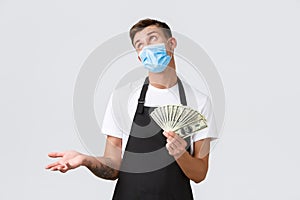 Small retail business, employees and coffee shop concept. Indecisive handsome barista, salesman in medical mask bragging