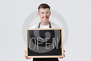Small retail business owners, cafe and restaurant employees concept. Charismatic smiling waiter, salesman holding open