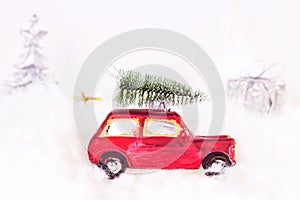 Small retro red toy car with green fir  tree on the top and presents on white artificial snow background. Christmas and New Year