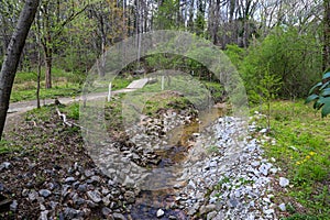 A small river flowing over rocks in the park surrounded by lush green trees, grass and plants at Murphey Candler Park