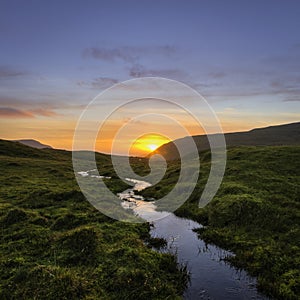 Small River Guiding the way to Sunset with Red Clouds and Blue Sky. (Faroe islands)