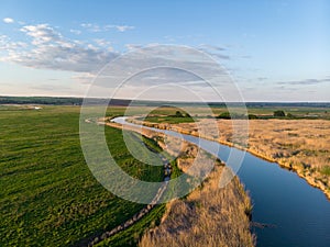 Small river meanders in the midst of green fields and meadows at sunset. Beautiful landscape with a bird`s eye view on a summer ev