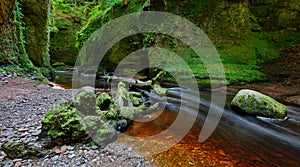 Small river with red water flowing through Finnich Glen landscape