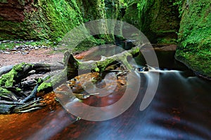 Small river with red water flowing through Finnich Glen landscape