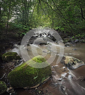 A small river with water rifts and a large stone covered with moss