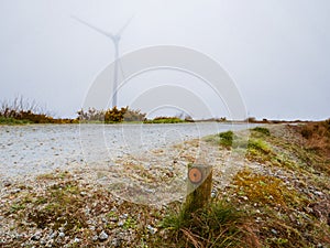 Small road in foreground and wind power turbine in the background in the fog. Green renewable power energy source