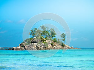 Small rocky island off the coast of the Seychelles with beautiful blue waters and sunhine.