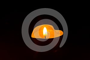 Small round candle with heart-shaped tablet is lit in the dark