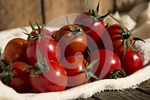 Small round cherry tomatoes with cuttings on a white napkin, wooden background. Delicious healthy vegetables, raw food