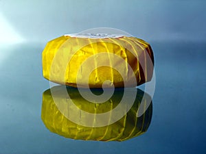Small round hotel soap in yellow paper wrap on glass surface with reflections