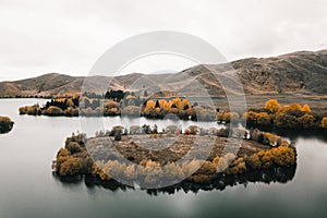 small round island with grass and trees on the edges in a lake in the middle of nature near the calm treeless mountains