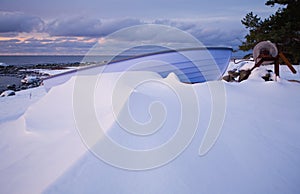 Small row boat laying on a pebble beach covered in snow