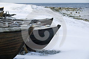 Small row boat laying on a pebble beach covered in snow