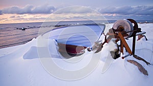 Small row boat laying on a pebble beach covered in snow