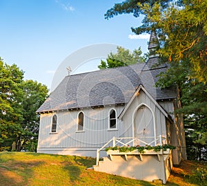 A small rural church in the woods, steeped in sunlight and shadow.