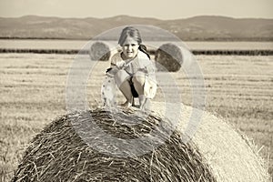 small rural girl on the straw after harvest field with straw bales