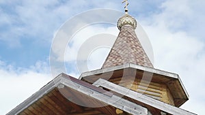 Small rural wooden church dome with golden cross against blue sky.