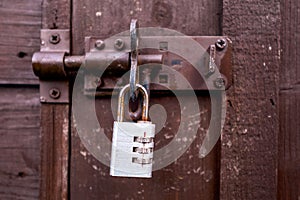 Small rusty metal code padlock on a metal latch and dark brown wooden door. Property safety and protection concept. Security