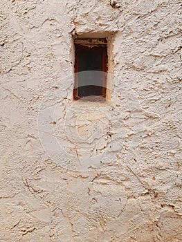 Small rusty window in old cement wall. Mud brick wall with window. Close-up of very old grungy weathered window. Architecture and