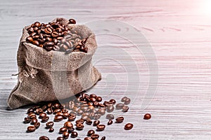 Small sack of coffee beans and some grains lying near it on the light background