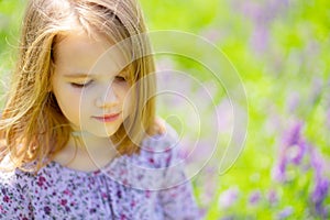Small sad girl alone in field of purple flowers. child is unwell because of heat