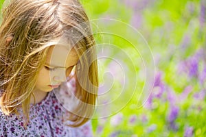 Small sad girl alone in field of purple flowers. child is unwell because of heat