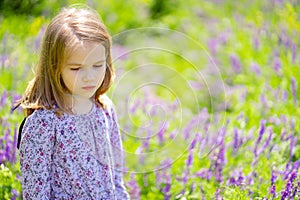 Small sad girl alone in field of purple flowers. child is unwell because of heat