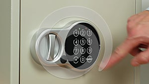 A small safe with an electronic code lock. The man`s hand opens the safe and takes last dollars